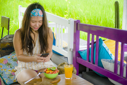 young happy and pretty digital nomad Asian Korean woman taking picture of fruit salad with mobile phone networking on internet social media