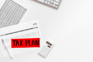 Tax plan words on office work desk with bills, keyboard, coffee, glasses on white background top view copy space