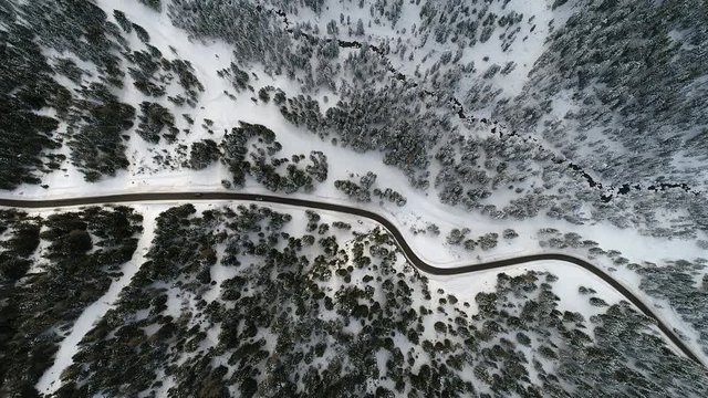 top view aerial drone flying above curvy road wind mountains and forest covered with snow on bad weather