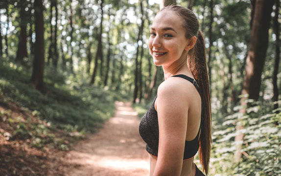 Smiling athletic woman before her run outdoors. Portrait of a young sporty woman smiling before training in the forest. Beautiful girl looking and smiling at the camera before run
