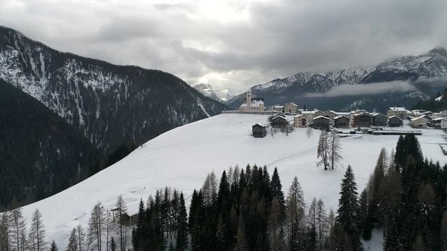 aerial drone flying above small church in italian alps at cludy winter day