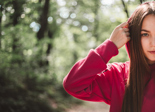 Beautiful sports female straighten a pink sweatshirt during training outdoors. Young attractive woman before activity in the forest. Cropped image of a sports caucasian female straighten pink clothes.