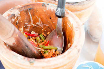 Hand of woman cooking spicy green papaya salad, carrot and herb in wooden mortar, Street food vendor make Som tam in Thailand, Thai papaya salad Som Tum, Thai style food.