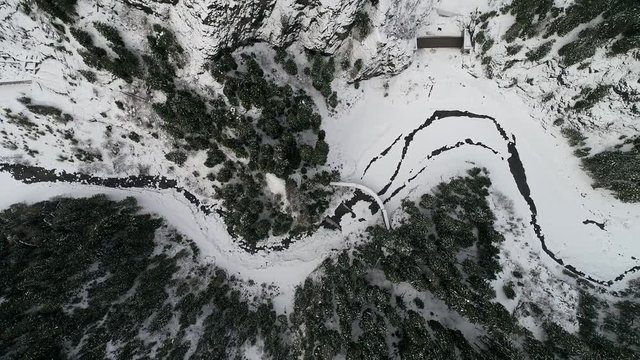 top view aerial drone flying above curvy road wind mountains and forest covered with snow on bad weather