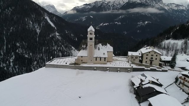 aerial drone flying above small church in italian alps at cludy winter day