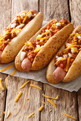 Delicious chili hot dogs with cheddar cheese, spicy beef mince, onion and sauce close-up. vertical, rustic