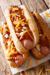 Chili hot dogs with cheese cheddar, spicy ground beef, onion and sauce close-up. vertical