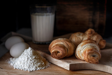 Fresh cooked croissants on cutting board with flour, milk, eggs. fresh pastry, bakery.
