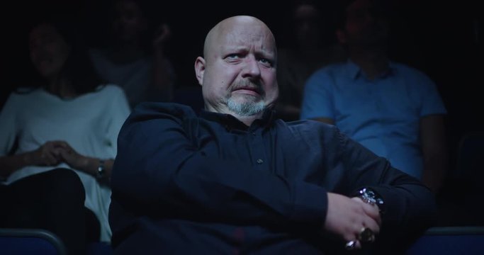 A scared reaction. A middle aged man cowers in his cinema seat struggling to watch a scary movie.