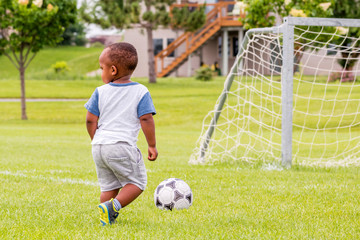 A little African toddler is playing soccer at summertime 