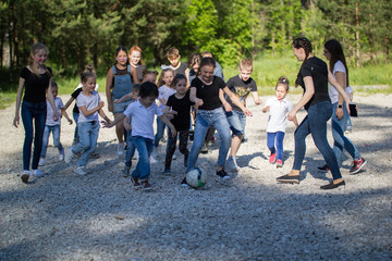 Team of teenagers playing yard football with a children team at sunny day
