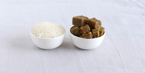 Sugar, which is a refined sweetener, and organic jaggery pieces, which are unrefined sweeteners, in bowls.