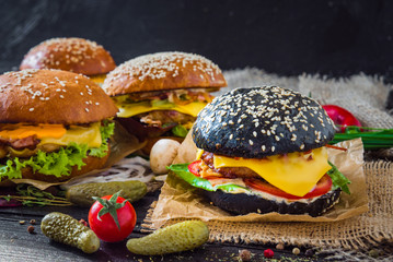 Black burger with beef stews, cheese, red cabbage and balsamic sauce served on small wooden chopping board over wooden table with black background.