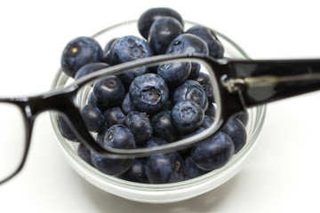 Bilberry cure for eyes concept with glasses. Glasses linse magnifying the blueberries