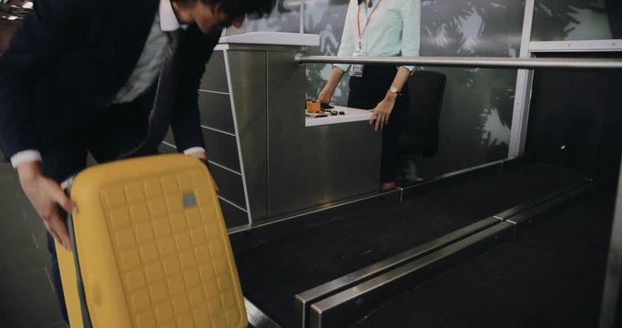 Young man weighing suitcase and doing check-in at airport