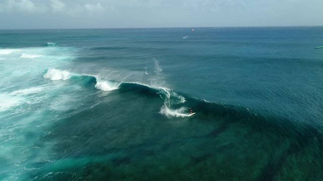 Kitesurfing Le Morne, Mauritius. Drone view flying backwards in front of kite surfer. Kite surfer surfing crystal clear water, perfect waves. Aerial view