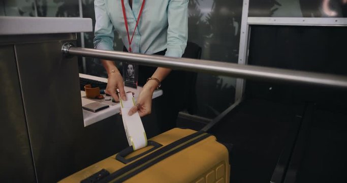 Young airline attendant attaching label on traveler's suitcase