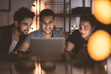 Group of smiling friends using laptop and uploading photos on Instagram