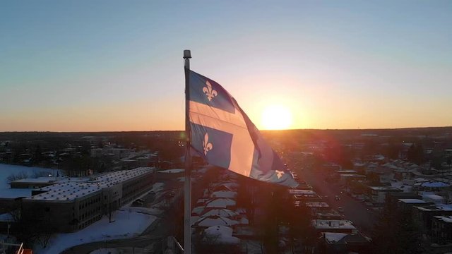 Slow motion drone view of the Quebec flag, with the sunset in the background