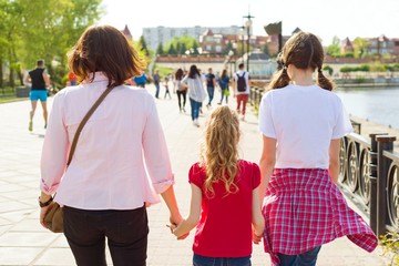 Outdoors portrait of mother and two daughters. Holding hands walking down the street, back view