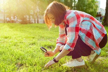 Adult woman with magnifier in the park looking at the grass