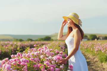 Beautiful young woman posing near roses in a garden.