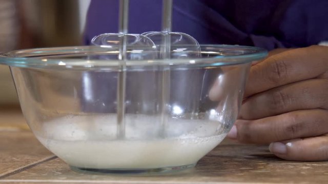 Isolated closeup of an electric mixer blending liquid in a glass bowl