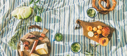 Fotobehang Picknick Platte zomerpicknickset met fruit, kaas, worst, bagels en limonade over gestreepte deken, bovenaanzicht, kopieerruimte