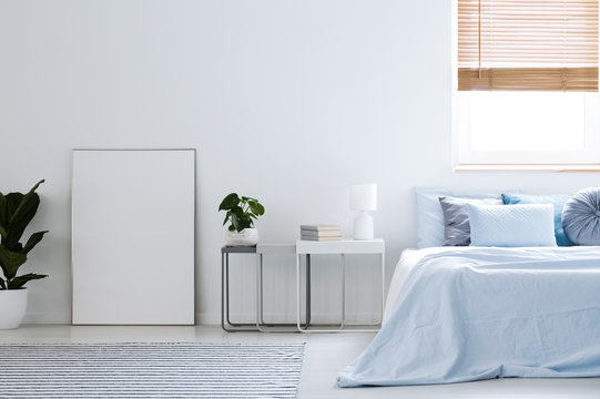 Mockup of white empty poster in simple hotel bedroom interior with blue bed. Real photo