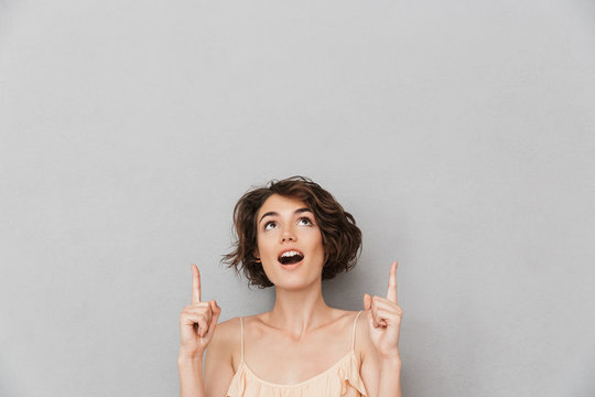 Portrait of a surprised young woman pointing fingers up