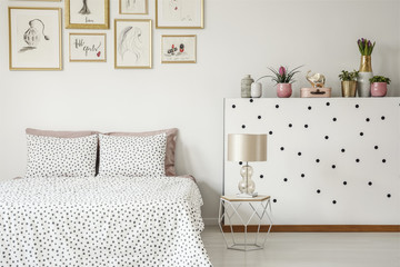 Elegant lamp on a diamond shape nightstand by a white wall with polka dot stickers and plants in a...