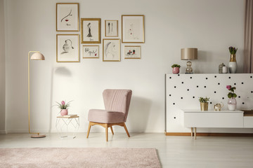 Old-fashioned armchair, pastel pink floor lamp and stylish, golden decorations in a retro living room interior with white walls - obrazy, fototapety, plakaty