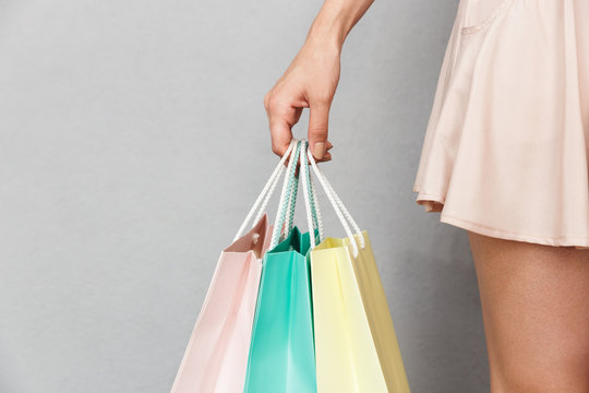 Cropped image of caucasian woman wearing skirt holding colorful paper shopping bags with purchases, isolated over grey background