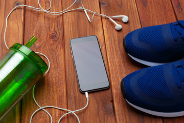 Sneakers and mobile phone with headphones on wooden table