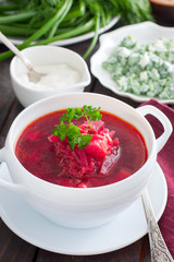 Vegetarian borsch with fresh herbs in a white serving plate, selective focus