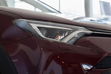 New vehicle of cherry color with elegant head lamps in showroom.