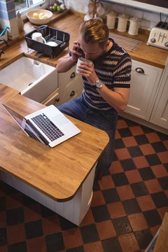 Man talking on phone while having coffee in kitchen