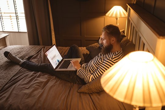 Man lying on bed while using laptop
