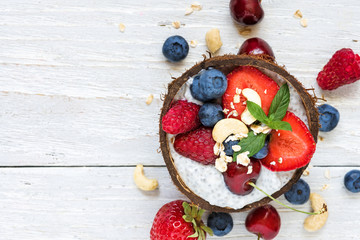 chia pudding with fresh berries, nuts, oats and mint in coconut bowl. healthy breakfast