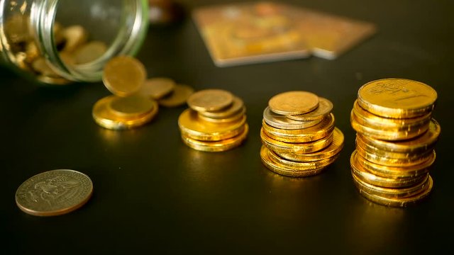 Saving money coin from jar. Symbol of investing, keeping money concept. Collecting cash conis in glass tin as moneybox. Close-up still life with increasing columns of gold coins on black table
