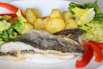 homemade dinner on a white plate baked potatoes fried fish cod, green lettuce with spices, and preserved red pepper