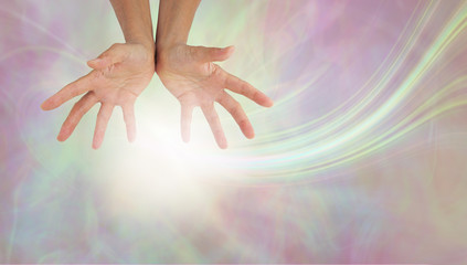 Sending out gentle healing energy- female hands against a pastel coloured etheral background with a...