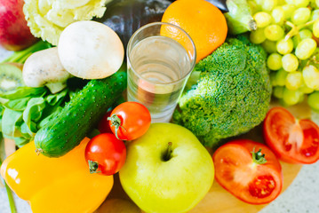 Many different fruits and vegetables with glass of water in the middle of