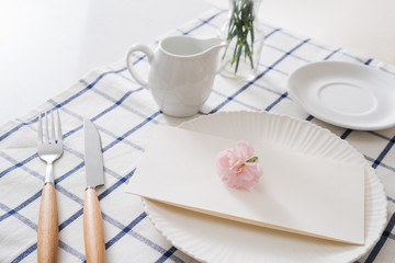 Table setting with dishes, cutlery and flowers on white background
