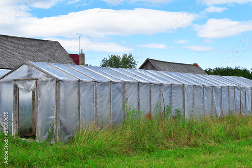 Plastic Greenhouse For Growing Vegetables And Greens On Farm Field Plastic Greenhouse For Growing Vegetables And Greens On Farm Field Overgrown In Long Grass