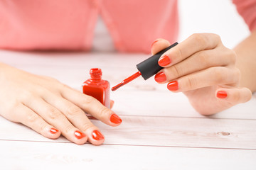 Obraz na płótnie Canvas Female hands with red manicure and an open bottle of varnish on the table