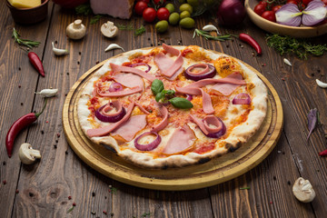 Delicious italian pizza with ham, sausages and onion decorated by basil leaves on wooden background