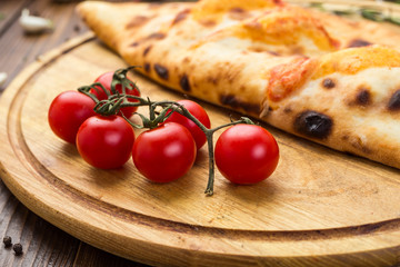 Traditional italian closed pizza Calzone with basil leaves on wooden background