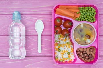 top view of tray with kids lunch for school and bottle of water on pink table