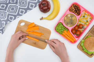 cropped image of mother preparing kids dinner for school and cutting carrot
